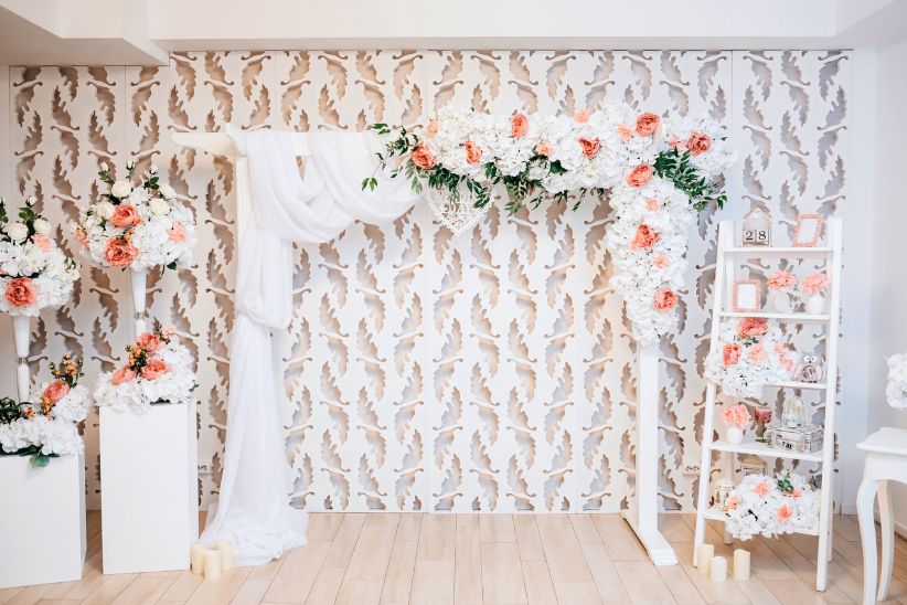 Indoor wedding photo booth zone decorated with white roses in vases, and old white table.