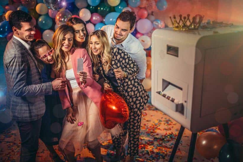 Group of young women and men having fun with balloons and photo booth at a party
