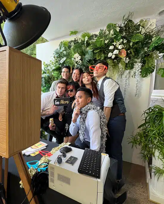 Group posing with props in a photo booth with floral backdrop in Orange County, CA