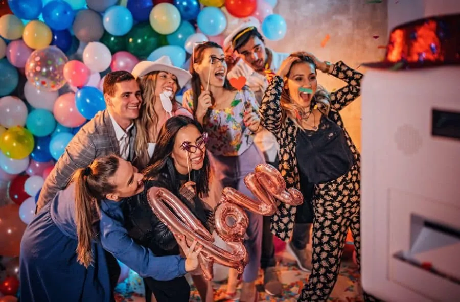 Group of friends enjoying a colorful photo booth rental with props and balloons.