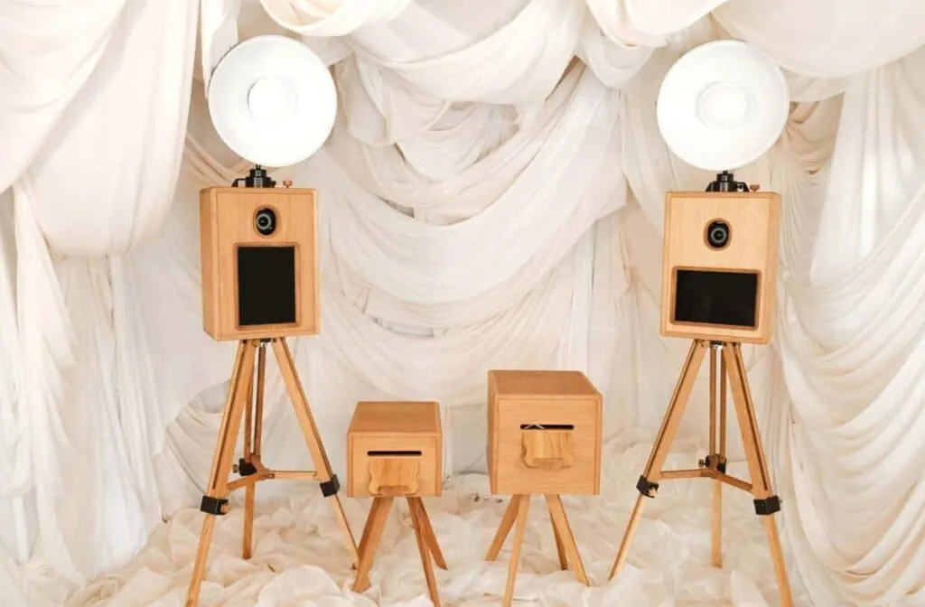 Wooden glam photo booth setup with twin cameras and soft draped white fabric backdrop.
