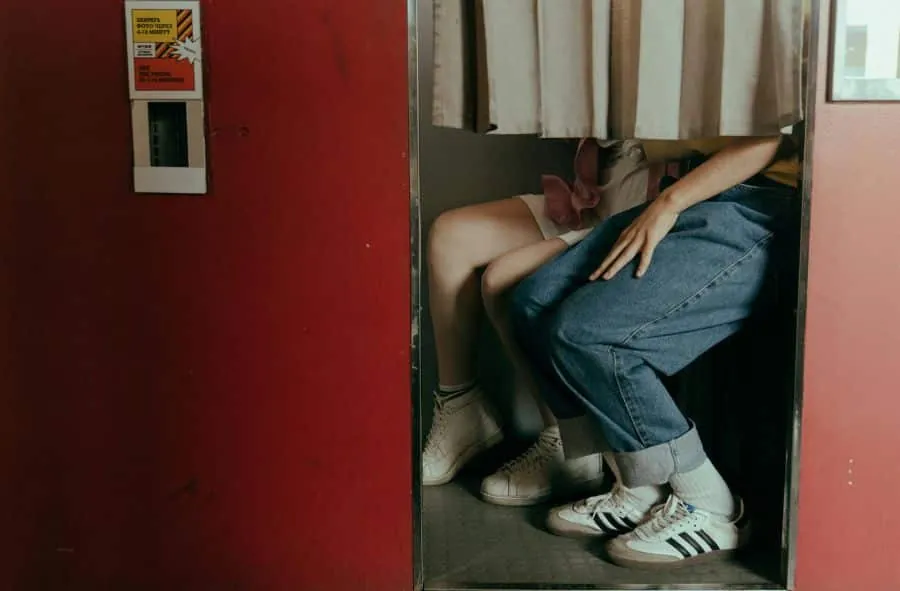 Couple seated inside a closed-curtain traditional photo booth, legs visible, capturing a moment together.