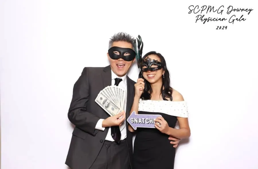Guests at a corporate event posing with masquerade masks, cash props, and a fun sign.