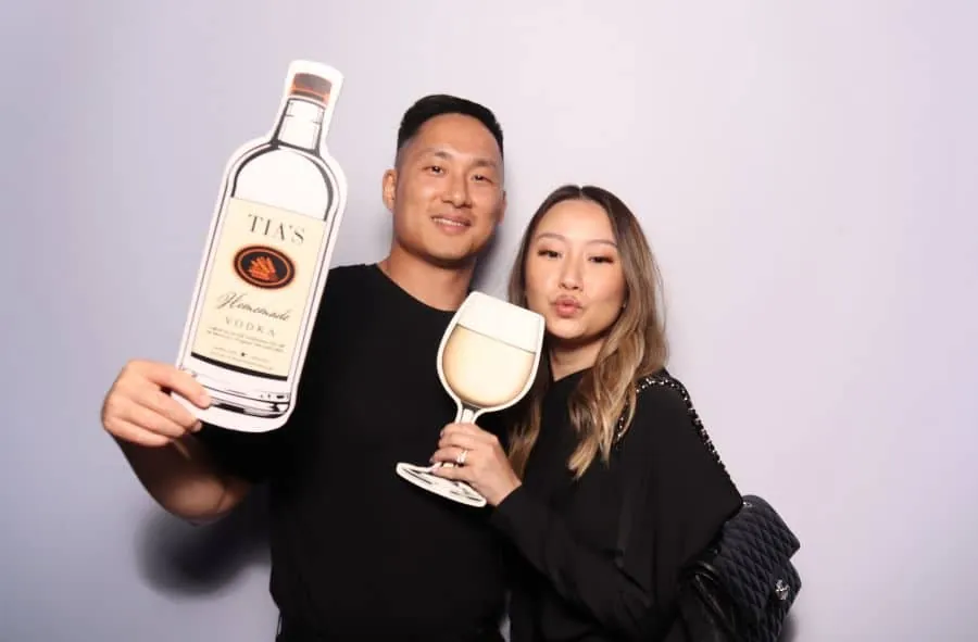 Couple posing in a wedding photo booth with vodka bottle and wine glass cutout props.
