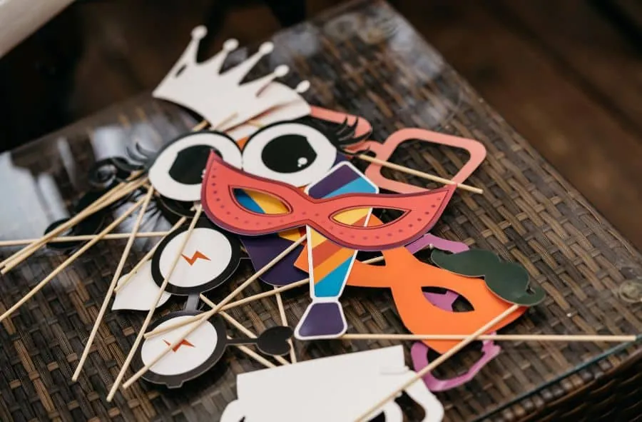 A variety of colorful DIY photo booth props, including masks, crowns, and glasses, laid on a table.