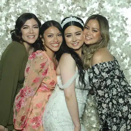 A bride posing with her friends in a photo booth, smiling against a sparkling sequin backdrop.