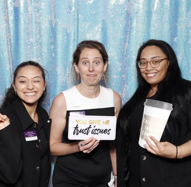 Three friends pose with playful props at a birthday party photo booth with a sparkling blue backdrop.