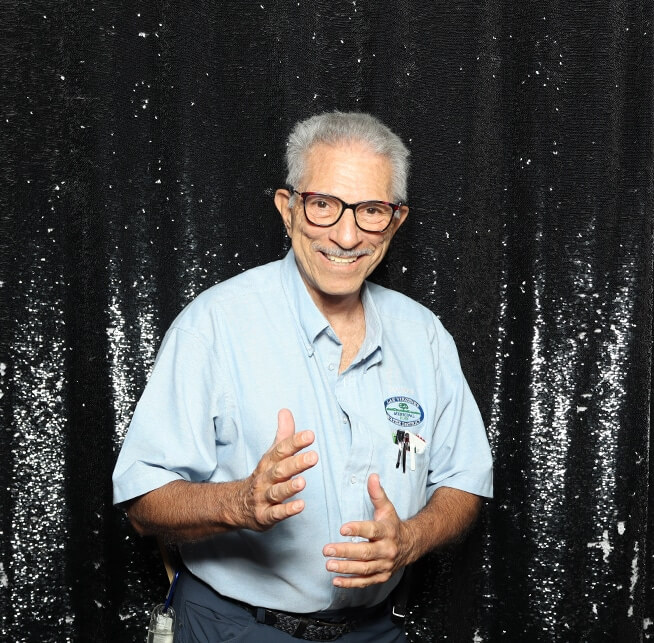 Smiling man in a light blue shirt poses playfully at a birthday party photo booth with a black backdrop.