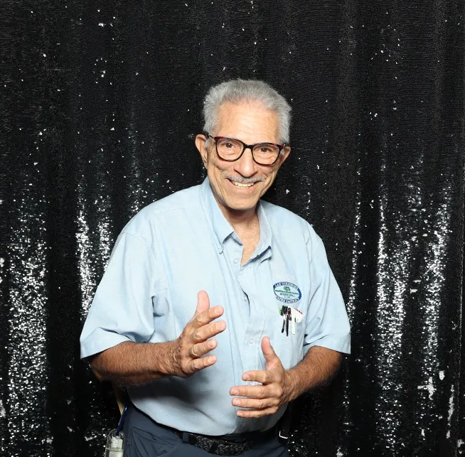 Smiling man in a light blue shirt poses playfully at a birthday party photo booth with a black backdrop.