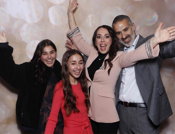 A joyful group poses with raised arms at a corporate photo booth with a sparkling bokeh backdrop.
