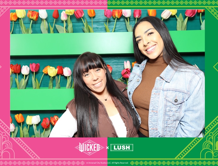 Two smiling women pose at a corporate photo booth with a colorful tulip backdrop and event branding.