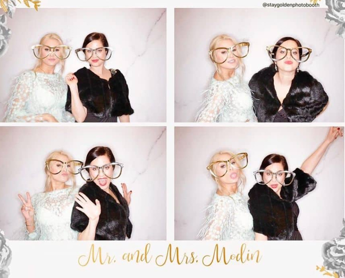 Two ladies pose playfully with oversized glasses at Mr. and Mrs. Modin's wedding photo booth.