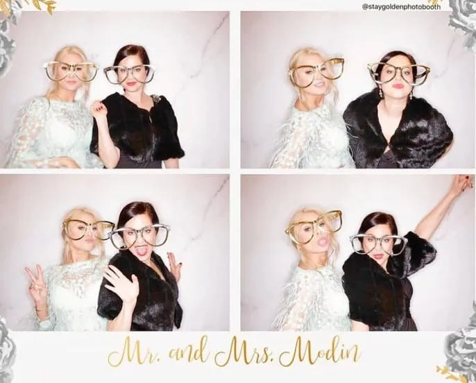 Two ladies pose playfully with oversized glasses at Mr. and Mrs. Modin's wedding photo booth.