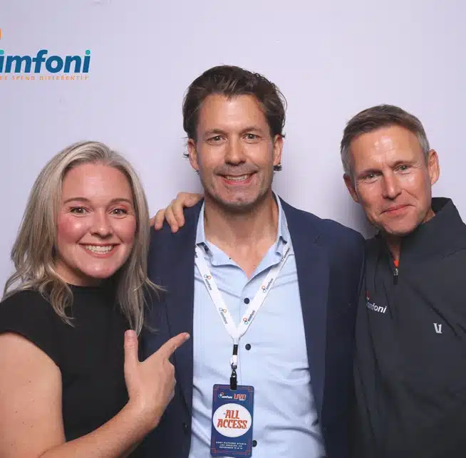 Three professionals pose at Simfoni’s conference photo booth, smiling with an "All Access" badge.