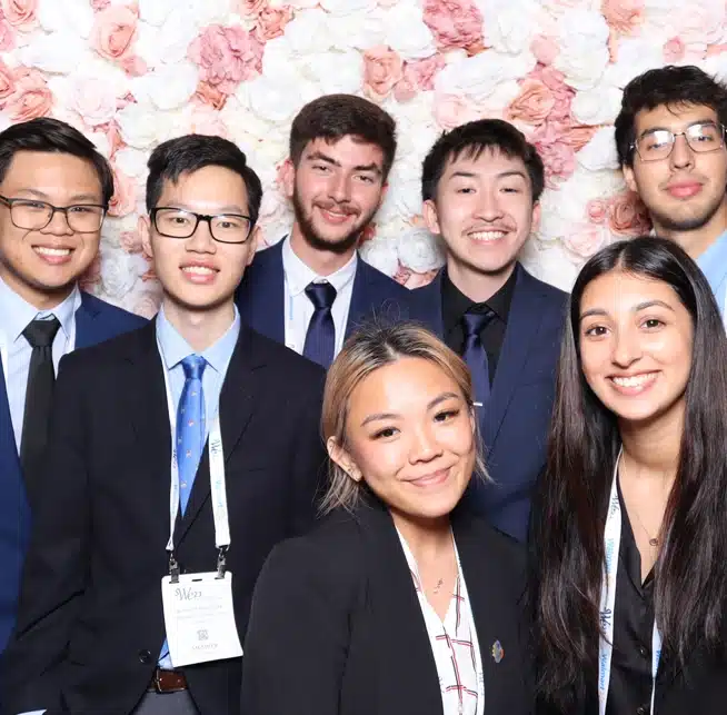 A group of professionals in business attire smiles at a corporate photo booth with a floral backdrop.