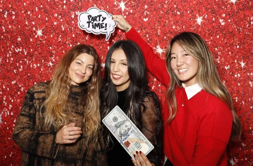 Three women posing at Happy Holidays Plus Development Group event with photo props and smiles.
