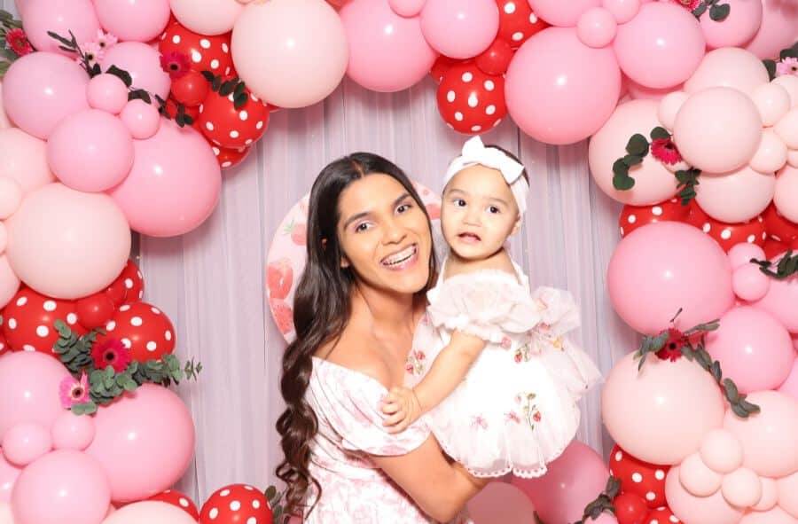 Mom and baby smiling in front of a pink and red balloon backdrop at Lavender’s Berry First Birthday.