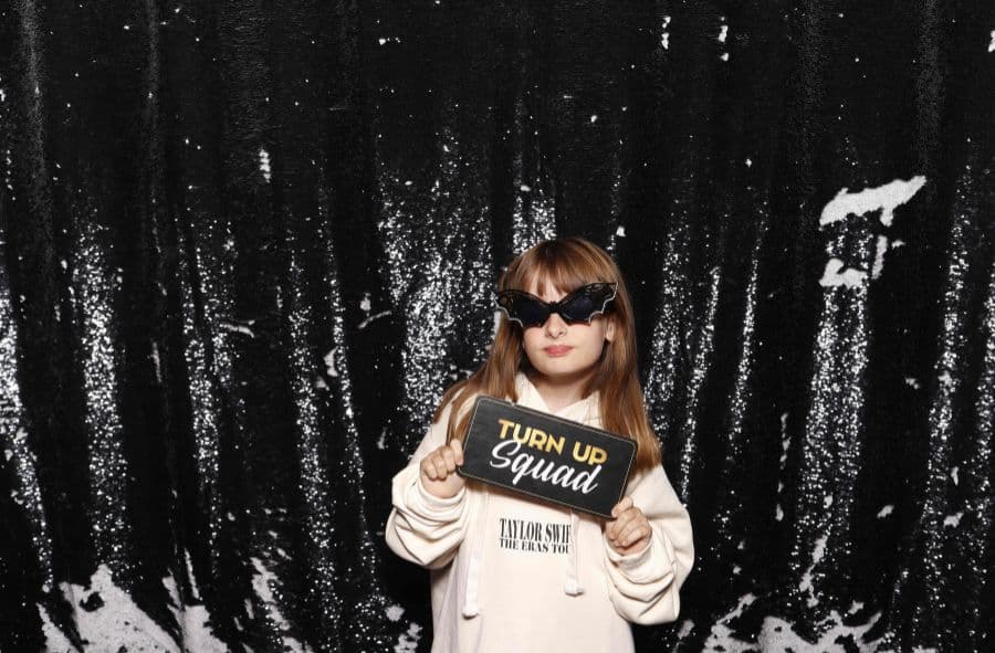 Girl in bat sunglasses holding a Turn Up Squad sign in front of a black sequin photo booth backdrop.