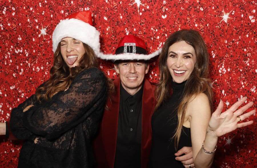 Three guests in holiday hats smiling and posing at Happy Holidays Plus Development Group party."