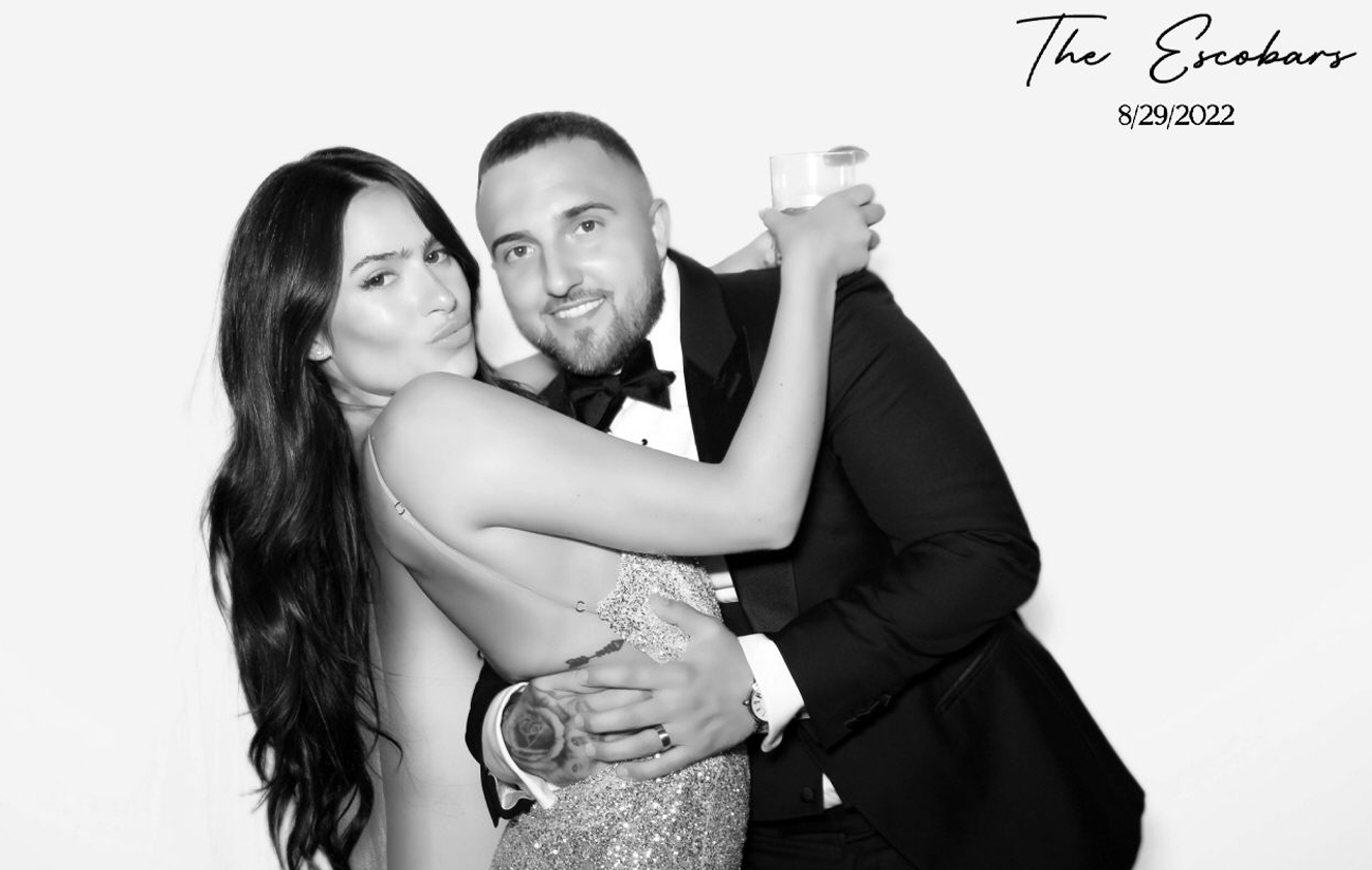 Newlyweds posing in a photo booth at their wedding with a black and white filter, dressed in elegant attire.
