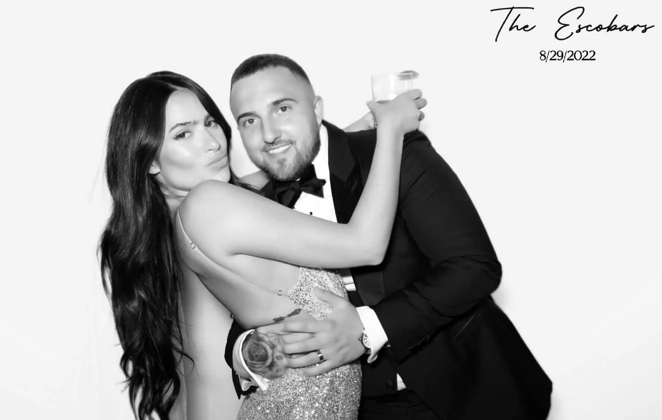 Newlyweds posing in a photo booth at their wedding with a black and white filter, dressed in elegant attire.