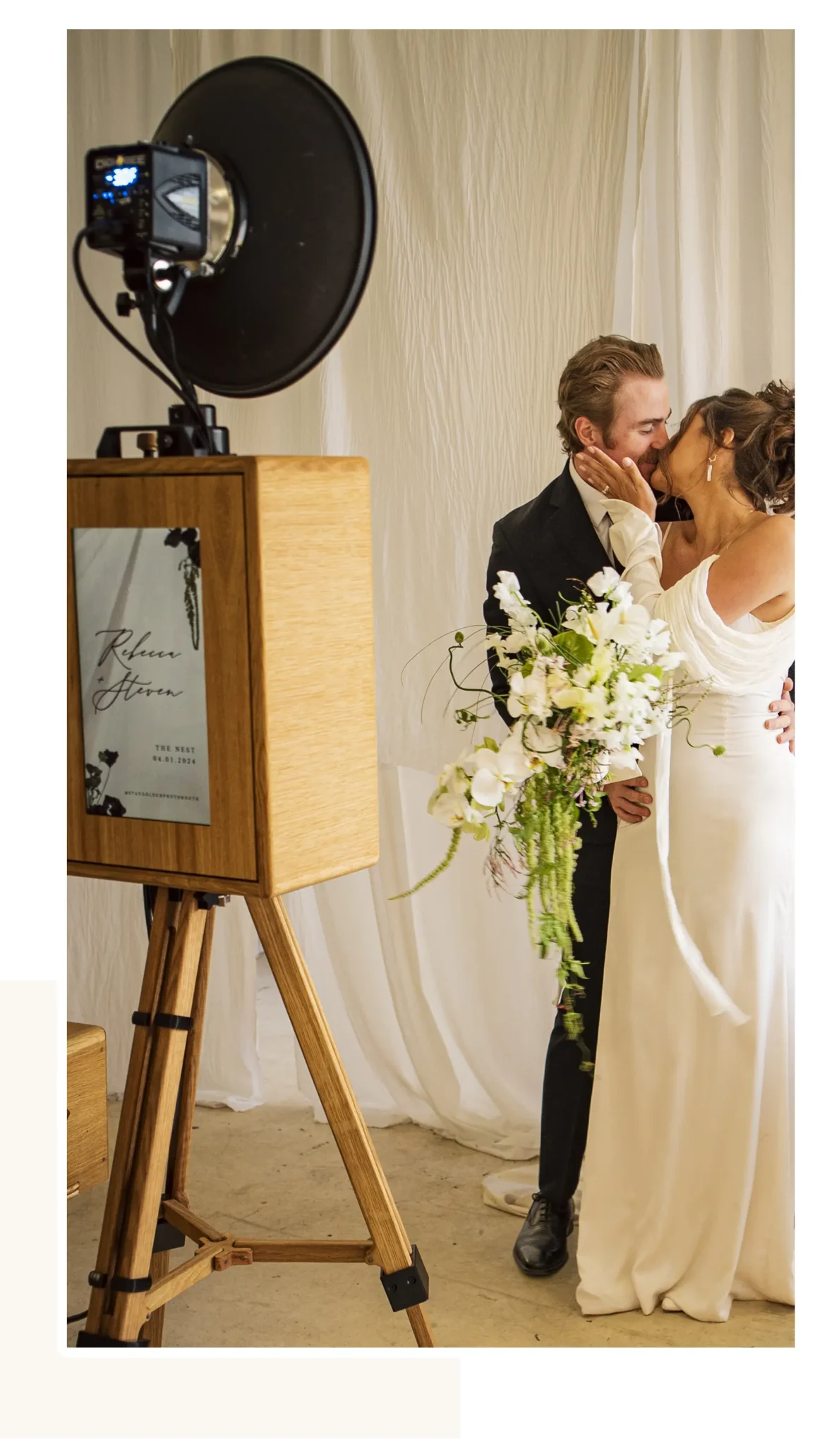 A newly married couple shares a kiss in front of a vintage-style photo booth capturing their special moment.