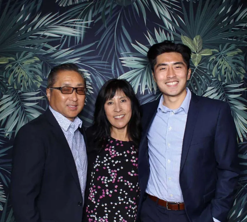 Group smiling in photo booth with tropical leaf backdrop at a formal event.