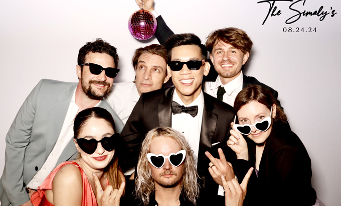 A group of guests in stylish outfits and sunglasses pose with a disco ball at The Smuly's photo booth.