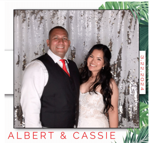 Smiling bride and groom posing in a digital mini photo booth with a silver sequin backdrop.