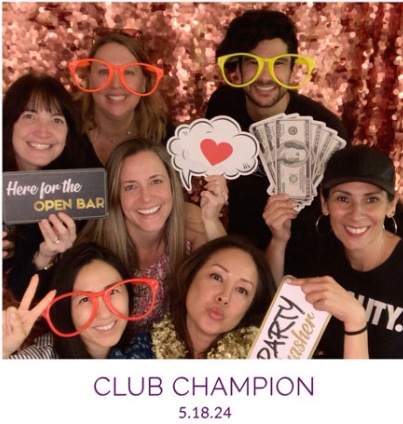 Group posing with props in a digital mini photo booth with a sparkling backdrop at a lively club event.
