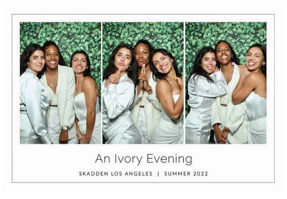 Group posing in a mirror photo booth with a greenery backdrop at a stylish event.