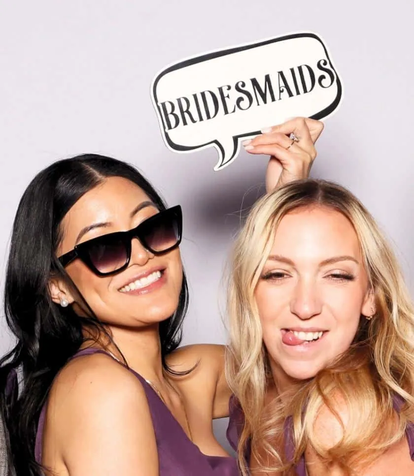 Two bridesmaids posing with a "Bridesmaids" sign at The Watkins' wedding photo booth rental in Long Beach.