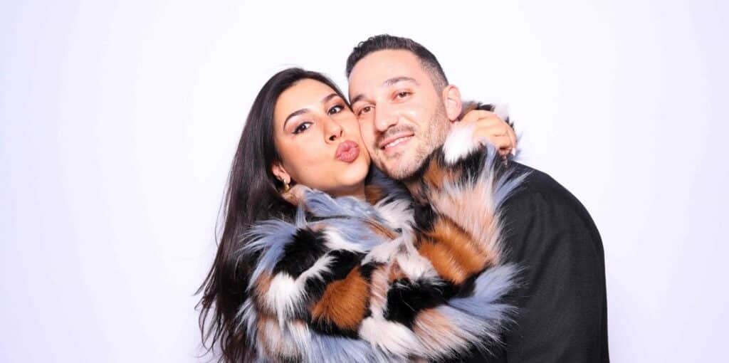 Stylish couple hugging and posing at Sasooness Law Group Holiday party in a photo booth rental in Riverside.