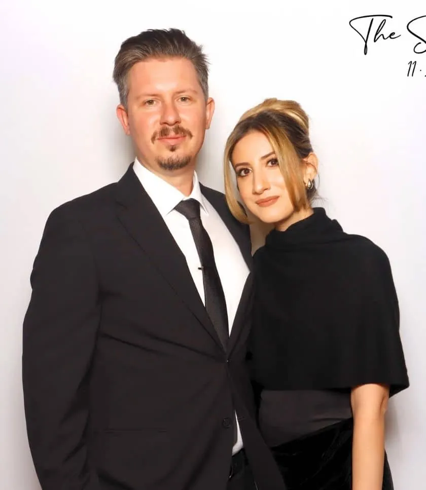 A well-dressed couple posing at a wedding photo booth in Torrance, smiling against a white backdrop.