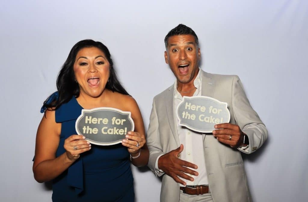a couple posing in a photo booth with "here for the cake" prop