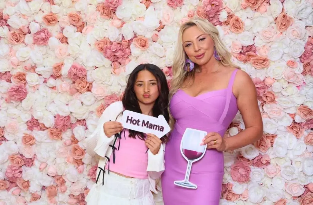 a mom and daughter pose for a photo in front of a floral backdrop