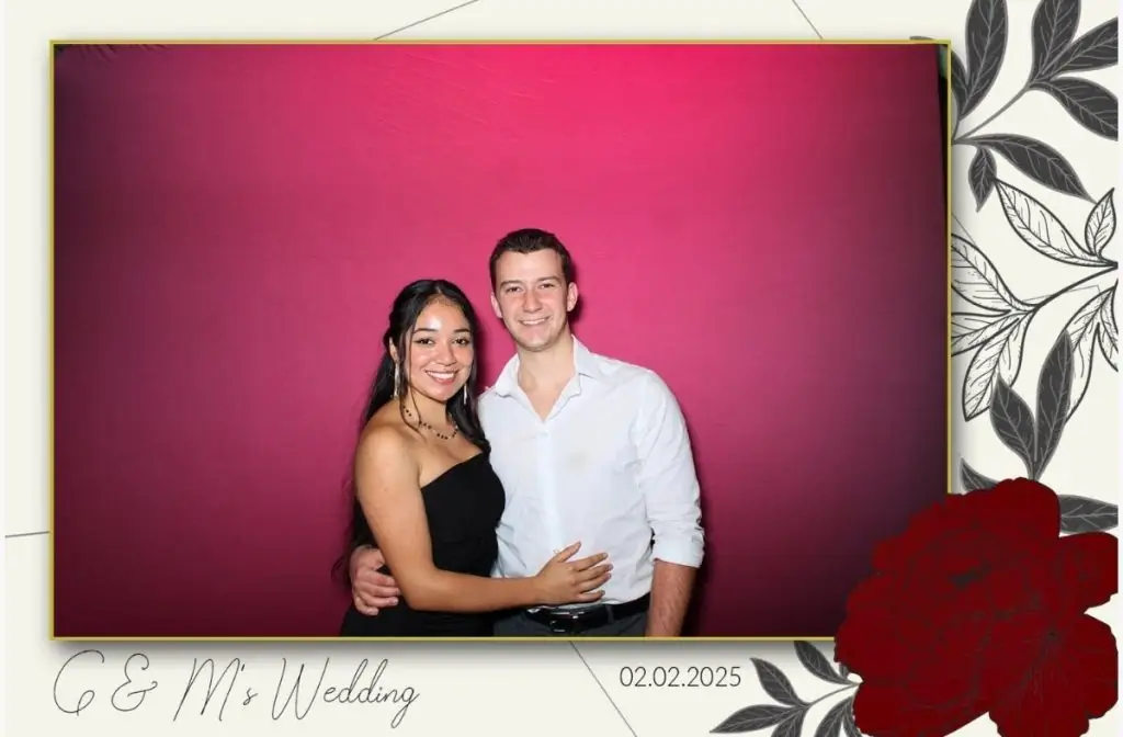 A couple posing for a wedding photo booth in front of a red backdrop