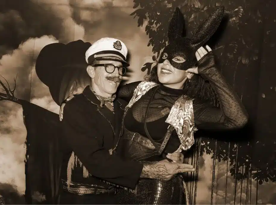 Man in a captain costume and woman in a bunny mask posing playfully in a Halloween photo booth.