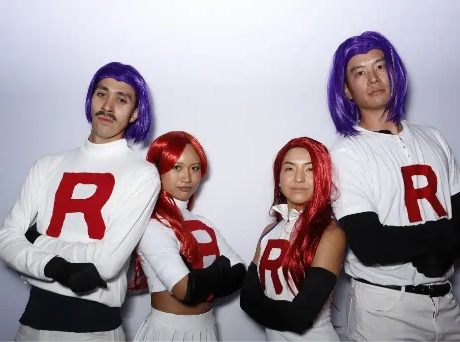 Group dressed as Team Rocket from Pokémon posing confidently with red wigs and white “R” shirts.