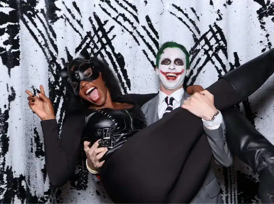 Man dressed as the Joker holding woman in Catwoman costume laughing together in a Halloween photo booth.