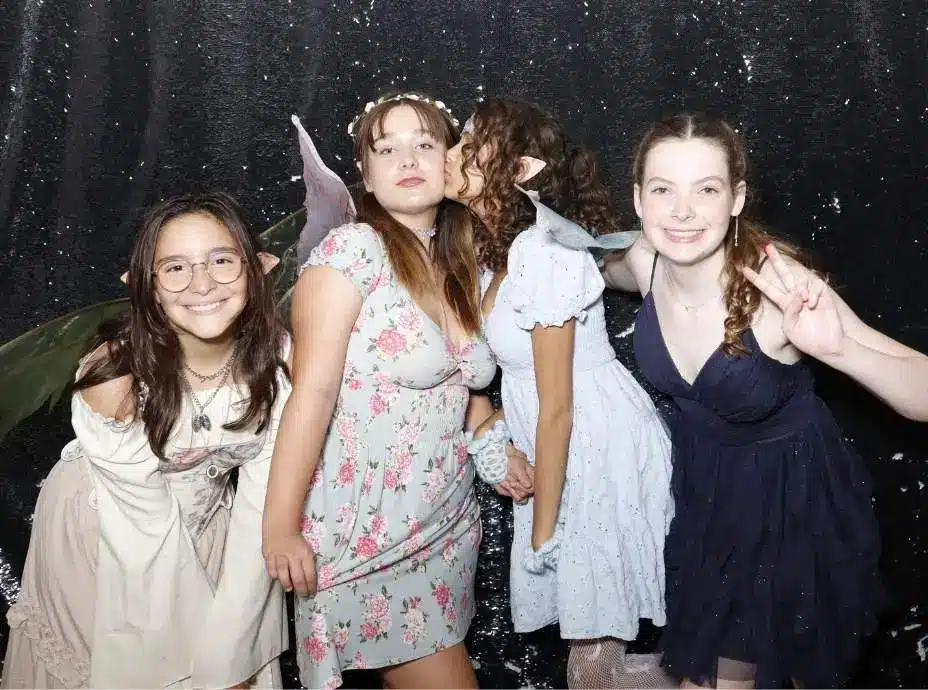 Group of girls dressed as fairies with wings and floral dresses posing playfully in a photo booth.