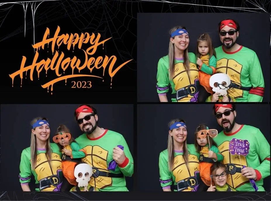 Family dressed as Ninja Turtles posing with fun props and smiles in a Halloween photo booth.
