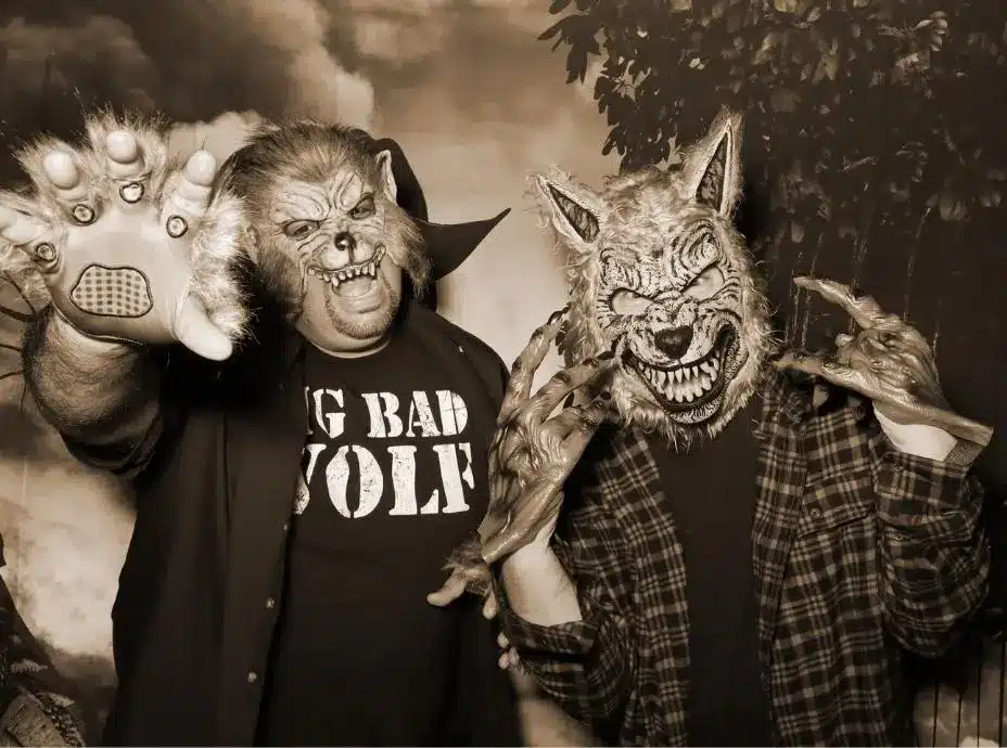 Two people wearing werewolf masks and claws posing fiercely in a Halloween-themed photo booth.