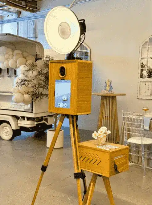 A Glam Photo Booth setup beside chairs and floral decor at a wedding indoor venue