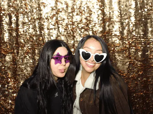 two ladies pose for a photo in front of a gold sequin backdrop