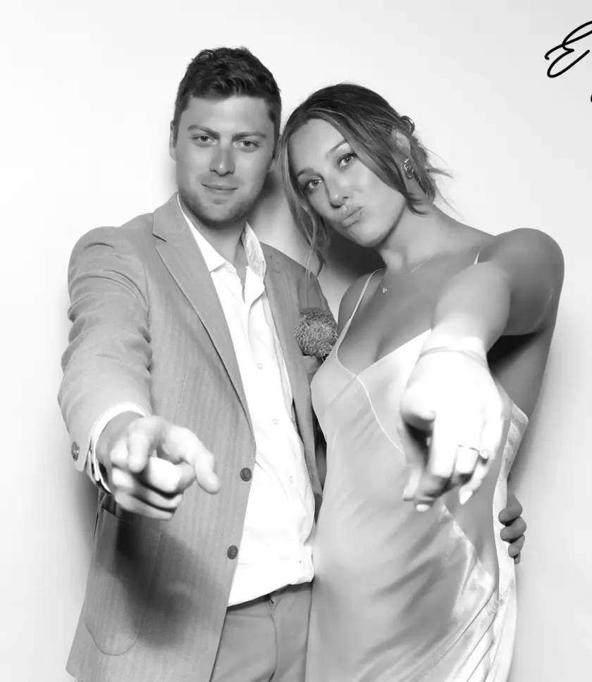 A couple poses for a glam photo booth, both pointing towards the camera with playful expressions.