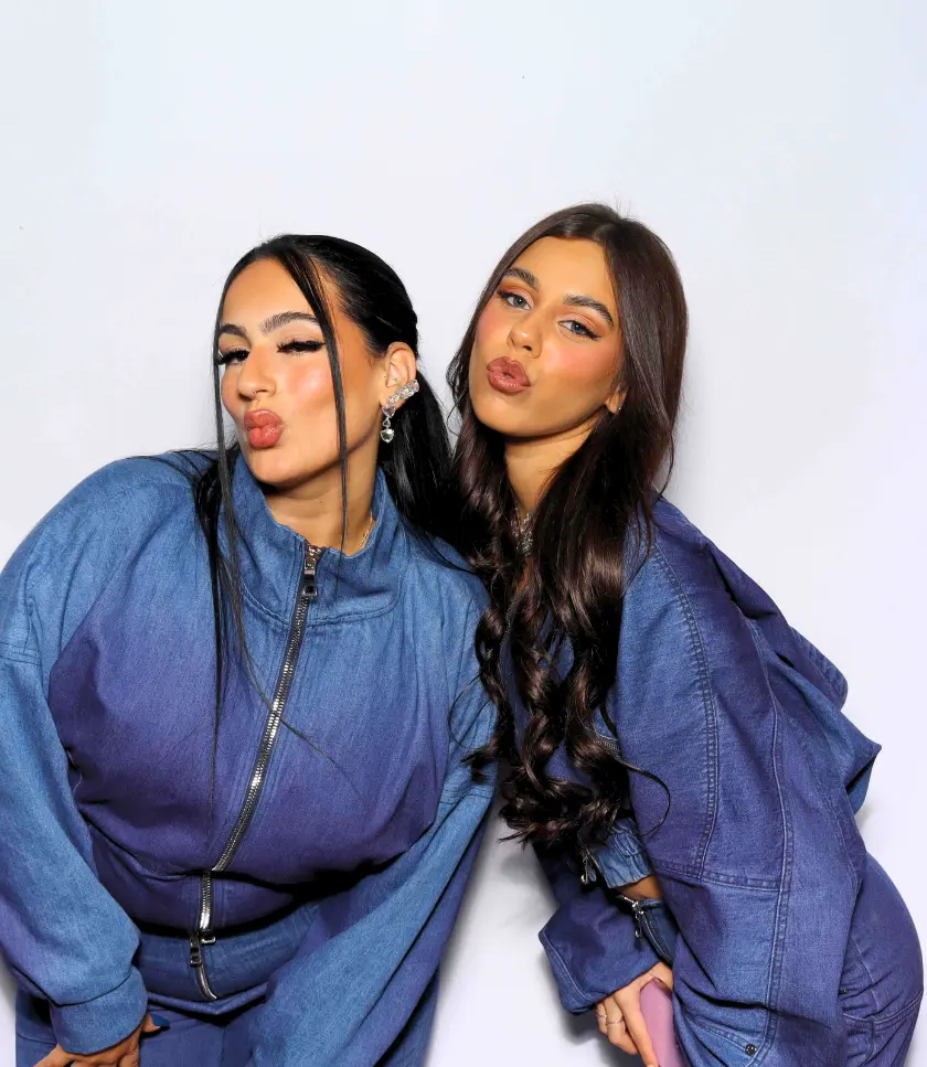 Two individuals wearing denim outfits with zippers, puckering their lips for a photo against a white background.
