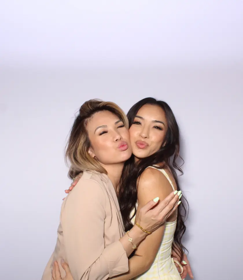 Two people embracing and puckering their lips against a white background infront of a photo booth.