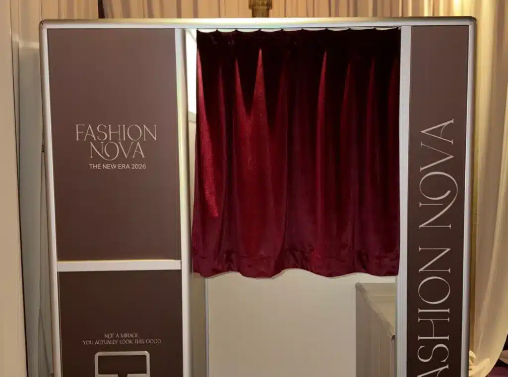 A "Fashion Nova" brand activation enclosed photo booth with a sparkly red curtain and a white counter inside.