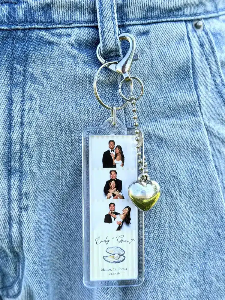 A keychain with a photo booth strip of a couple, a silver heart charm, and text reading "Emily & Street" and "Malibu, California".